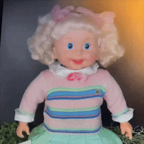 a doll wearing a pink and blue striped sweater has a kiss on her cheek