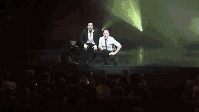three men are kneeling on a stage in front of a crowd of people
