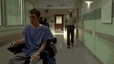 a man in a hospital gown is walking down a hallway next to a boy in a wheelchair