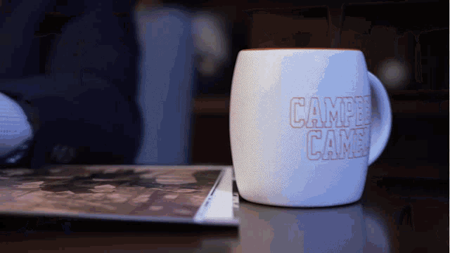 a coffee mug that says campers came sits on a table next to a magazine