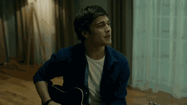 a man in a blue shirt is playing a black guitar