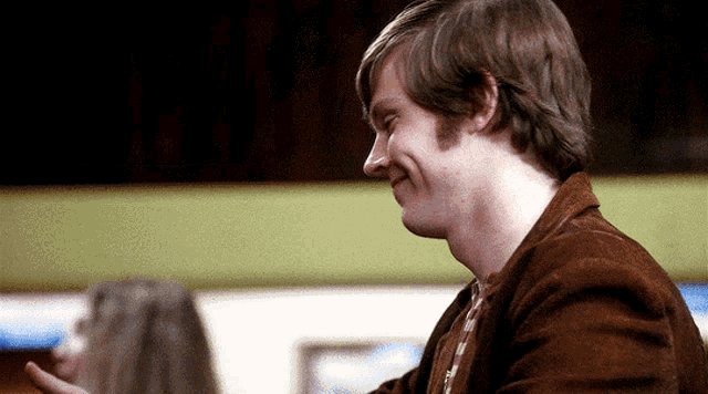 a man in a brown jacket is smiling while looking down