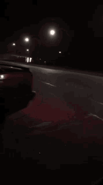 a red car is driving down the street at night