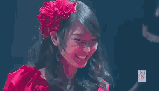 a woman wearing a red dress and a red flower in her hair is smiling and making a peace sign .
