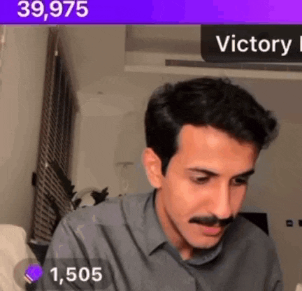 a man with a mustache is sitting in a living room with a purple sign that says victory .