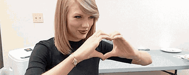 a woman is making a heart with her hands while sitting at a table .