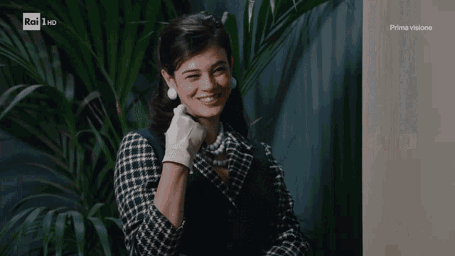 a woman wearing a plaid jacket and white gloves is smiling in front of a tv screen that says rai hd prima visione