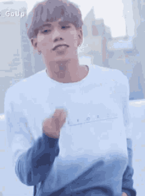 a young man with gray hair is wearing a white t-shirt and a gray sweater .