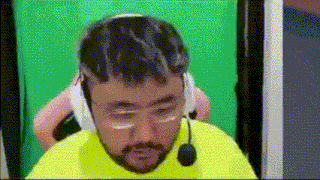 a man with a beard wearing headphones and a microphone is sitting in front of a green screen .