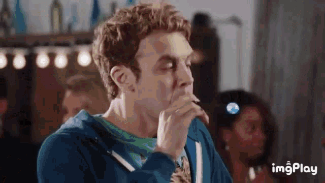 a man in a blue sweatshirt and tie is drinking from a bottle .