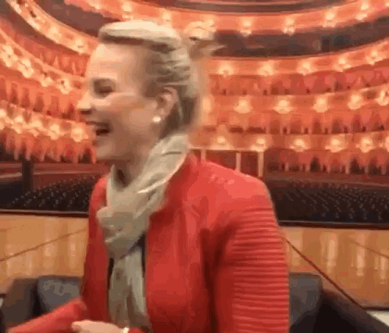 a woman in a red jacket and scarf is laughing in front of a large empty auditorium .