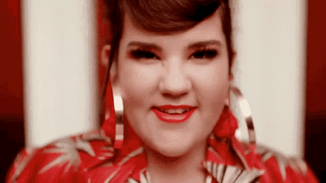 a woman wearing a red shirt and red earrings is smiling .
