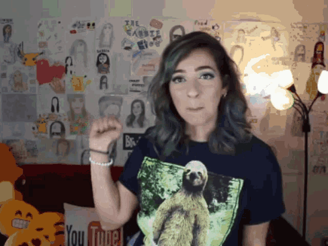 a woman wearing a t-shirt with a sloth on it is standing in front of a wall with drawings on it