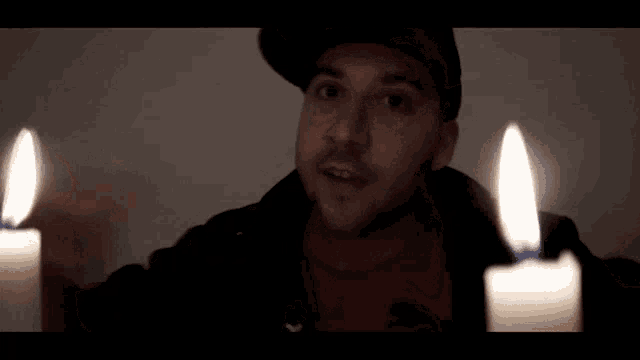 a man is sitting in front of two lit candles and covering his face