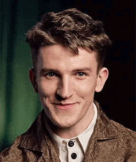 a young man wearing a brown jacket and white shirt is smiling for the camera .