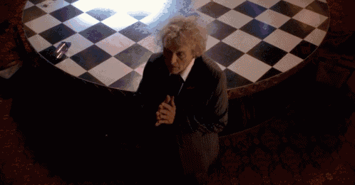 a man sits in front of a checkered floor with his hands folded