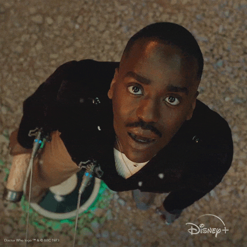 a man in a black jacket is looking up at the camera with a disney logo behind him
