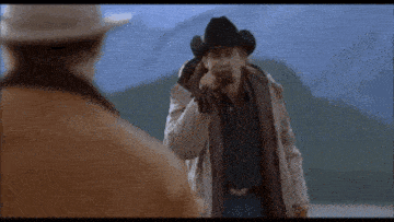 a man in a cowboy hat holds a gun in his right hand