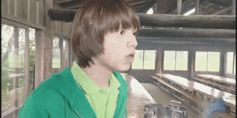 a young boy wearing a green jacket and a green shirt is standing in a room with long tables .