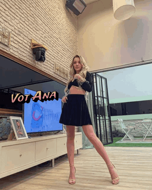a woman in a black dress is standing in front of a tv with vot ana written on the bottom right