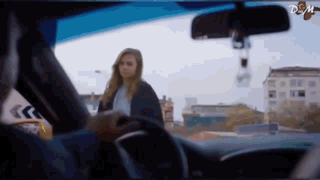 a man is driving a car with a woman standing in front of him .