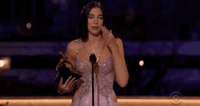a woman in a pink dress is holding a trophy and speaking into a microphone on a stage .