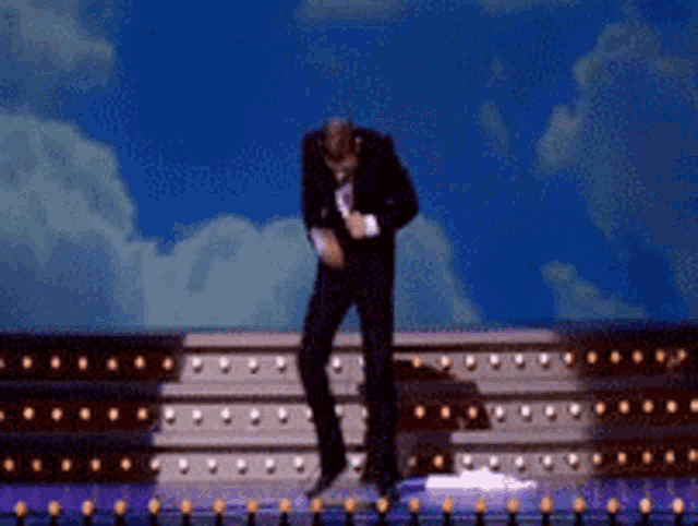 a man in a suit is dancing on a stage with a blue sky in the background