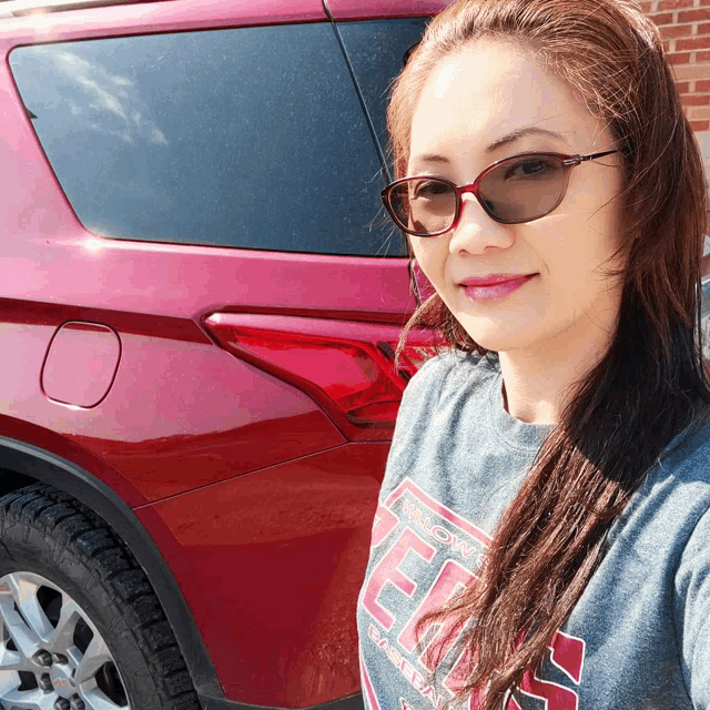 a woman wearing sunglasses and a shirt that says texas is standing in front of a red suv