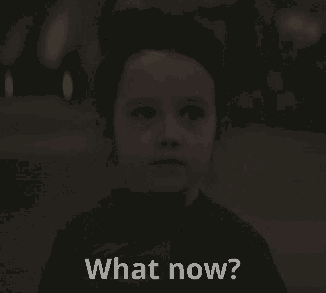 a little girl is looking at the camera with the words " what now " below her