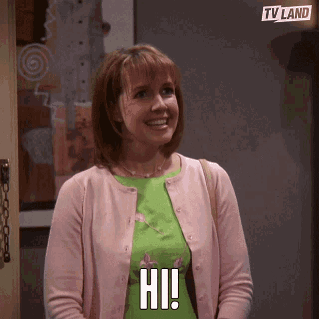 a woman in a pink cardigan is smiling and says hi