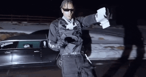 a man standing in front of a black car holding papers