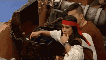 a man and a woman dressed as pirates are looking at a treasure chest .