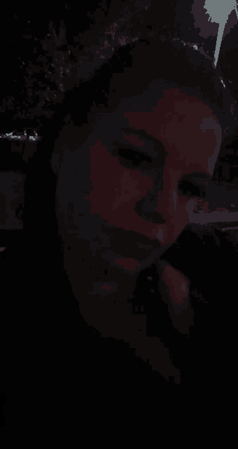 a close up of a woman 's face at night with a street light in the background