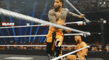 a man is holding a rope in a wrestling ring while another man is kneeling down .