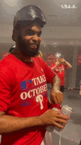 a man with a beard wearing a red shirt and a helmet is holding a can of soda .