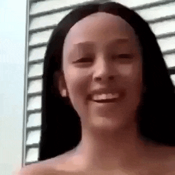 a woman with long black hair is smiling and looking at the camera while standing in front of a window .