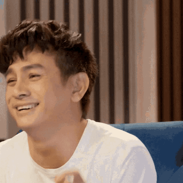 a young man in a white shirt is smiling and sitting on a blue couch