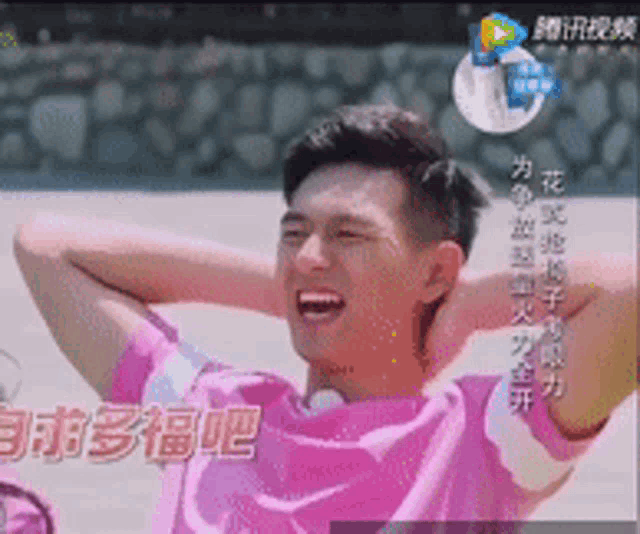 a man in a pink shirt is smiling with his hands behind his head