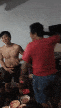 a man in a red shirt is standing next to a shirtless man in black shorts in a room .