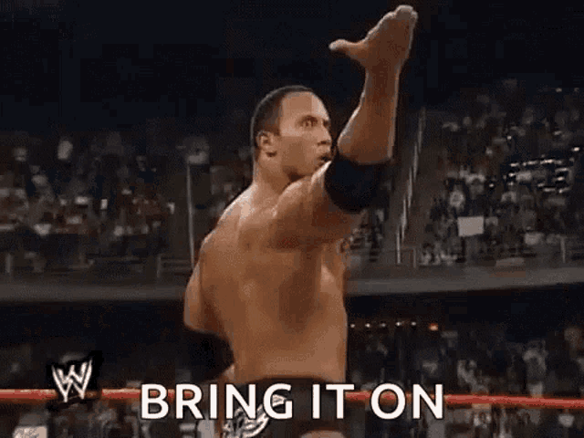 a wrestler is raising his fist in the air in front of a crowd and says `` bring it on '' .