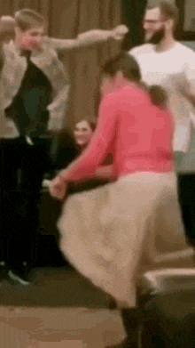 a woman in a red sweater and a tan skirt is dancing with a group of people .