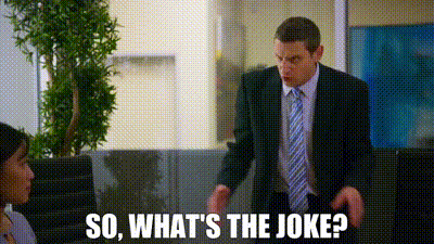 a man in a suit and tie is standing in front of a woman in an office and talking to her .