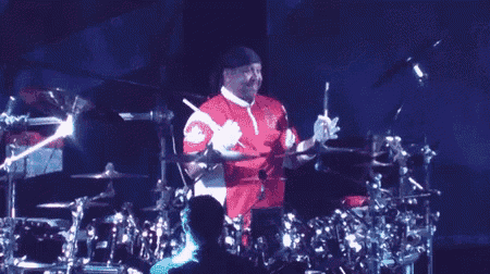 a man in a red and white shirt is playing drums on a stage