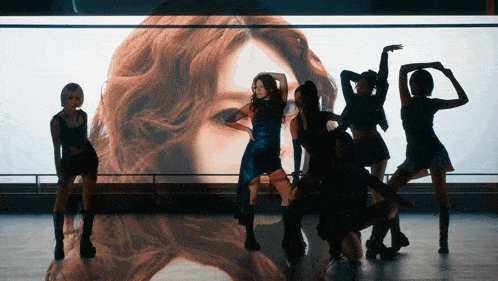 a group of women are dancing in front of a large image of a woman