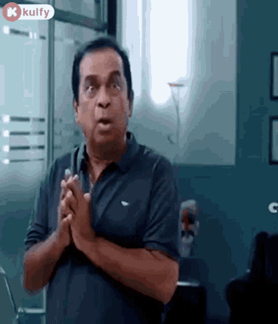 a man in a black shirt is standing in a room with his hands folded in front of him .