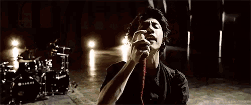 a man is singing into a microphone with his hands folded in front of his face .