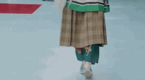 a model walks the runway at a fashion show wearing a plaid skirt and a sweater .