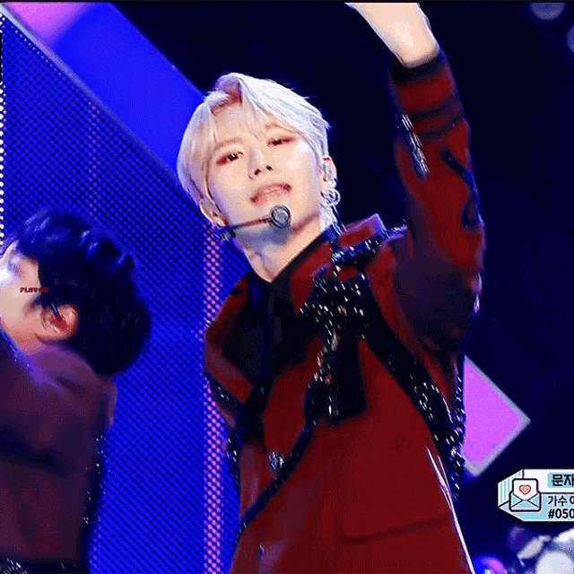 a man in a red jacket is singing into a microphone while another man looks on