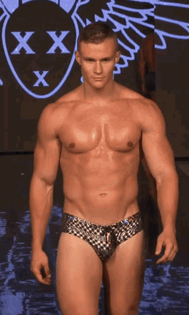 a man without a shirt is walking down a runway in front of a screen that says xxx