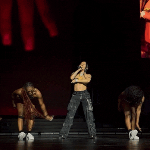 a woman is singing into a microphone while two dancers are dancing behind her